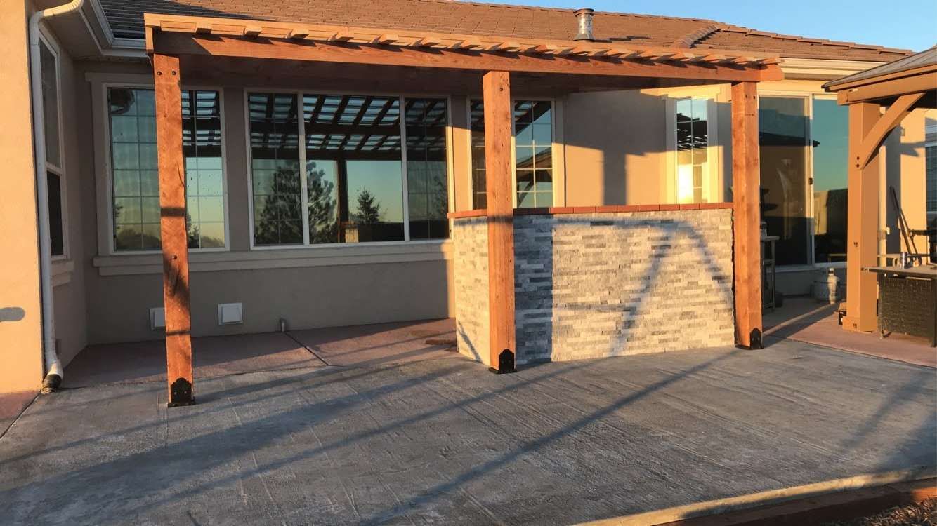 Cedar pergola with split-face stone half-wall over stamped-concrete patio